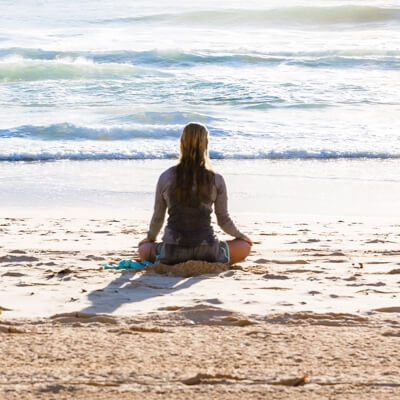 A woman sitting on a beach in the waves meditating.